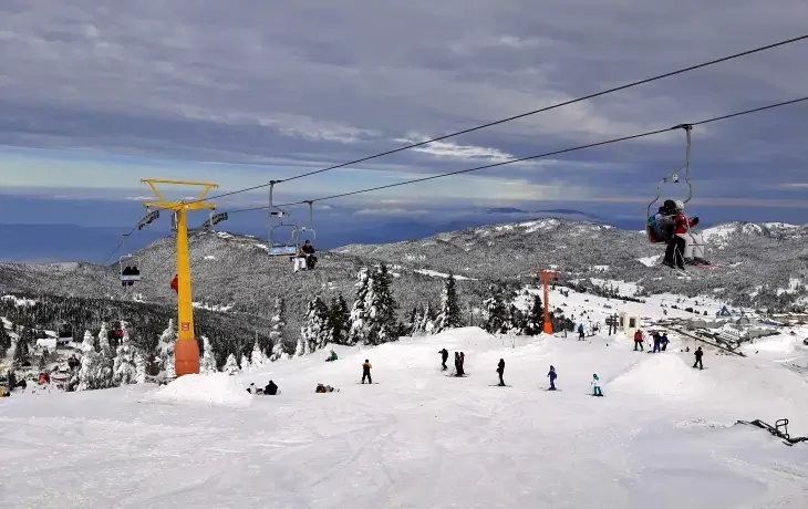 Uludağ Kayak Merkezi’nde telesiyej hattı, karla kaplı pistler ve kayak yapan ziyaretçilerle kış manzarası